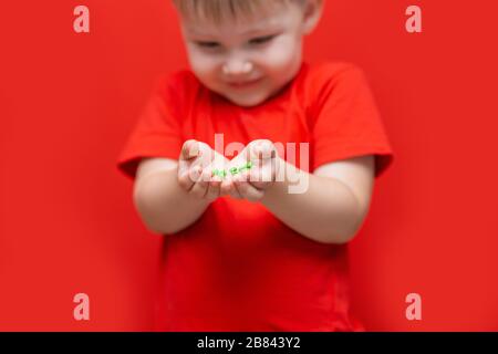 petit garçon triste enfant tenir beaucoup de pilules dans les mains. t-shirt rouge, fond rouge dangereux concept, comprimés et bébé Banque D'Images