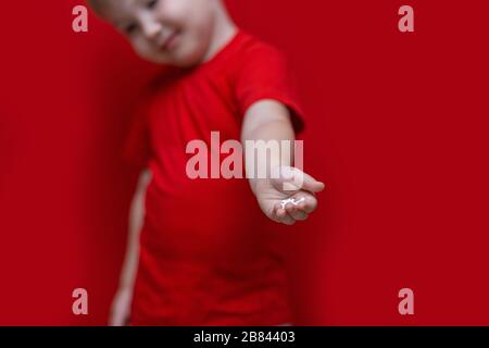 petit garçon triste enfant tenir beaucoup de pilules dans les mains. t-shirt rouge, fond rouge dangereux concept, comprimés et bébé Banque D'Images