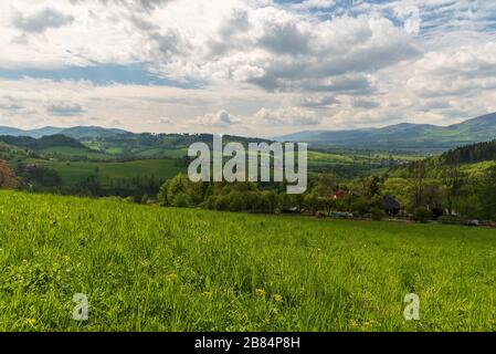 Paysage roulant autour du village de Vendryne en république tchèque avec collines, prés, arbres, colonie dispersée et ciel bleu avec nuages Banque D'Images