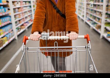 Jeune femme avec panier d'épicerie et étagères avec épicerie dans un magasin Banque D'Images