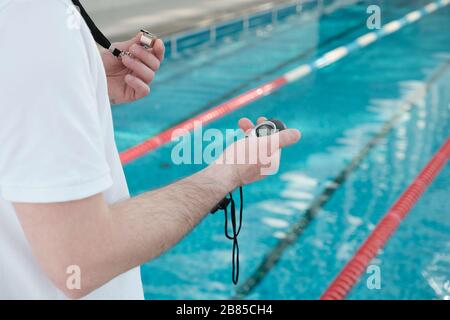 Gros plan d'un entraîneur non reconnaissable tenant sifflement et utilisant un chronomètre à l'entraînement de natation Banque D'Images