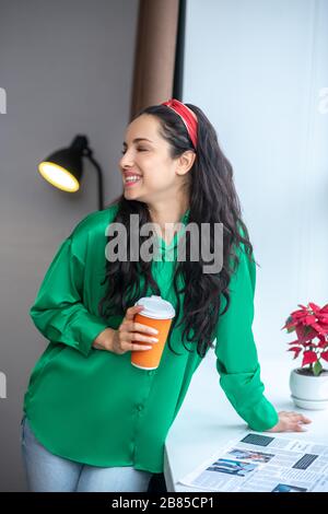 Femme dans un chemisier émeraude avec un verre de café. Banque D'Images