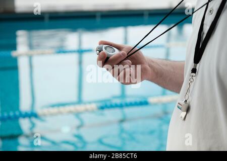 Gros plan d'entraîneur non reconnaissable avec sifflement à l'aide du chronomètre tout en déterminant les performances des athlètes dans la piscine Banque D'Images