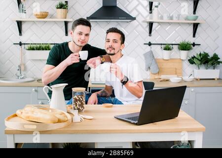 Deux hommes gais heureux dans la maison passer le matin dans la cuisine. Joyeux gay hommes prenant le petit déjeuner à la maison le matin. Banque D'Images