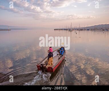 Les pêcheurs partent à la collecte des captures des pots. Lever du soleil au-dessus du lac de Genève pendant que l'équipage et leur petit bateau sortent du rivage pour vérifier leurs prises Banque D'Images