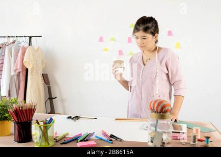 Le concepteur des vêtements est en méditant. Nouveaux vêtements de style pour la saison changeante, le design de l'équipement de couture est placé sur le bureau. Banque D'Images
