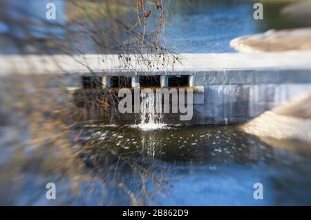 Paysage printanier avec un barrage cellulaire et une petite chute d'eau encadrée par des branches Banque D'Images