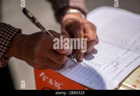 (200320) -- KUNMING, 20 mars 2020 (Xinhua) -- Villager Wang Daxiang s'inscrit pour obtenir les clés de sa nouvelle maison après son arrivée dans la zone de réinstallation de Maojiawan pour les pauvres du comté de Ludian, dans le sud-ouest de la province du Yunnan en Chine, 15 mars 2020. Niché au fond des montagnes de la province du Yunnan, dans le sud-ouest de la Chine, le village de Luoqiu ne compte que des dizaines de foyers qui se dispersent dans la vallée de la montagne. Le villageois Yan Fugao et sa femme Wang Daxiang vivent ici depuis plus de 20 ans. Un environnement montagneux difficile ici a sévèrement restreint les activités économiques des populations locales et en a causé une partie Banque D'Images