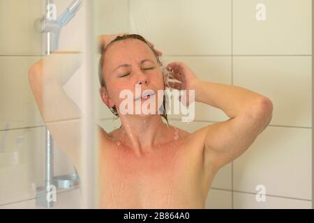 Femme hispanique d'âge moyen ayant une douche chaude rinçant le shampooing hors de ses cheveux sous l'eau courante dans un concept d'hygiène personnelle dans un po de gros plan Banque D'Images