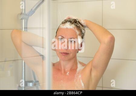 Jolie femme hispanique d'âge moyen se lavant ses cheveux avec du shampoing dans une douche dans un concept d'hygiène personnelle Banque D'Images