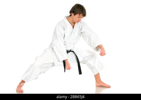 Un jeune homme de talent professionnel en karaté dans un costume kimono avec ceinture noire montre une position de combat posant sur un fond blanc. Espace publicitaire Banque D'Images