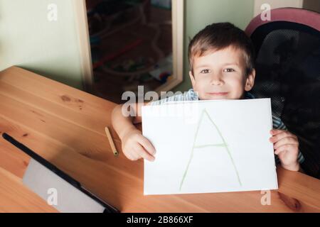 Heureux satisfait garçon montre la page avec la lettre écrite A, l'éducation à la maison Banque D'Images