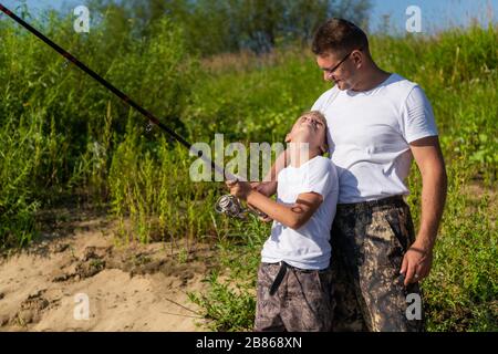 Un tel petit poisson. Père et fils qui étirent une canne à pêche avec du poisson sur le crochet alors que le petit garçon a l'air triste. Banque D'Images