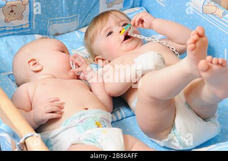 Deux nouveau-nés dans des couches couchées dans un lit de bébé en bois sur une couverture bleue avec mamelons de bébé dans la bouche Banque D'Images