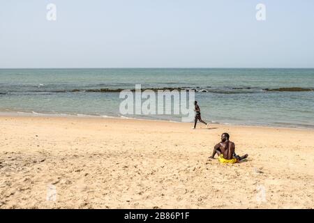 Saly, Sénégal. 19 mars 2020. Un homme est assis comme un autre court sur une plage presque vide qui était rempli de touristes à Saly, Sénégal, 19 mars 2020. Les touristes se rendant en avion pour retourner en Europe, les magasins, les hôtels et les marchés ferment progressivement à Saly, la station balnéaire du pays. L'éclosion de COVID-19 a un impact important sur l'industrie touristique du pays. Selon le Ministre sénégalais des transports aériens et du tourisme Alioune Sarr, Sénégal, tous les vols internationaux de passagers seront suspendus vers minuit vendredi. Crédit: Eddy Peters/Xinhua/Alay Live News Banque D'Images