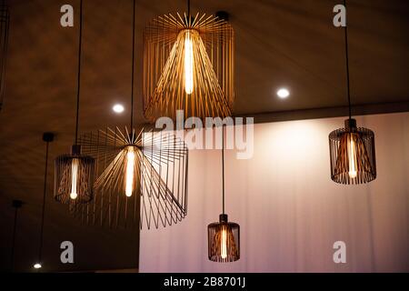 Chandeliers de carcasse de fil géométrique de différentes tailles. Abat-jour métalliques modernes sur un plafond sombre et un fond de mur clair. Lampes avec lumières lumineuses Banque D'Images