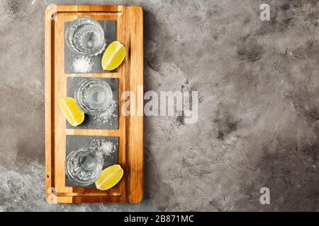 Tequila projectiles, limes et sel sur planche en bois sur fond gris. Vue de dessus, espace de copie Banque D'Images