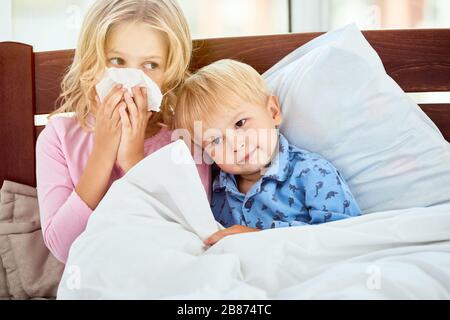 Petite sœur et frère avec nez liquide souffrant de grippe ou de froid tout en allongé ensemble à la maison. Maladie virale. Concept de coronavirus. Famille malade à la maison. Concept de santé Banque D'Images