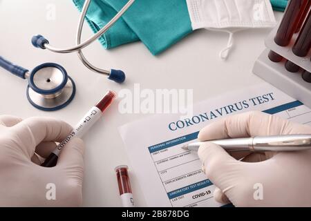 Médecin remplissant le formulaire de test de coronavirus sur le banc de laboratoire avec des échantillons de sang à analyser. Vue de dessus. Banque D'Images