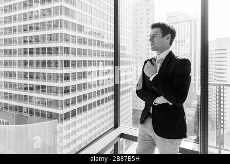 Un jeune homme d'affaires se tenant contre une fenêtre en verre avec vue sur la ville Banque D'Images