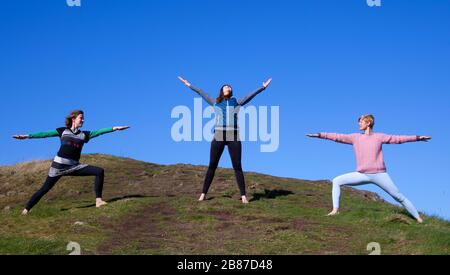 Holyrood Park, Édimbourg, Écosse, Royaume-Uni. 20 mars 2020. Ensoleillé, et température de 6 degrés centigrade, encourage ces jeunes dames à (avec l'espace approprié) prendre un certain temps pour respirer et méditer tout en pratiquant des exercices de yoga dans l'air frais, assurant de garder leur distance sociale les uns des autres. Photo : de gauche à droite, Jennifer, Belinda et Anna de WanderWomen Scoland. Banque D'Images