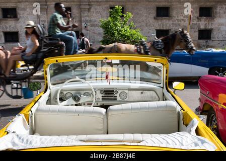 Voiture américaine convertible jaune d'époque garée et autocar à cheval passant par. Scène de la rue de la Havane, Cuba. Banque D'Images