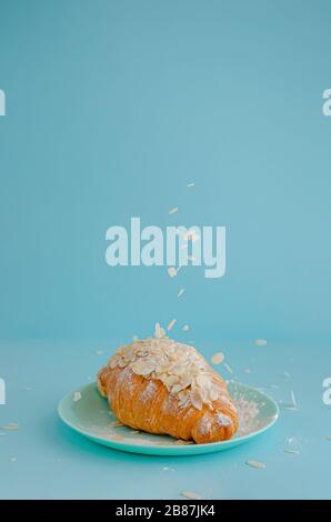 Flocons d'amandes de tomber sur des croissants adossés sur fond bleu. L'espace de copie, à la verticale. Banque D'Images