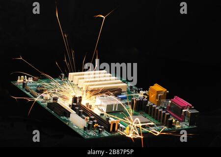 Des étincelles brûlantes s'envolent de la puce d'équipements électroniques complexes sur le fond sombre. Concept d'équipement de soudage en usine. Création d'une puce Banque D'Images