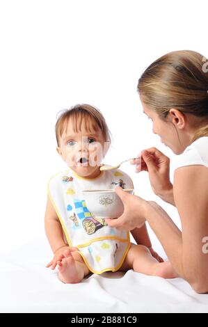 La mère nourrit une petite fille d'un an de nourriture de bébé ou de porridge avec cuillère. Les enfants mangent. Fond clair Banque D'Images