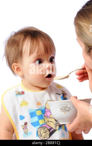 La mère nourrit la petite fille surprise de la nourriture de bébé de la cuillère. Soins parentaux et bonne enfance. Isolé sur fond blanc Banque D'Images