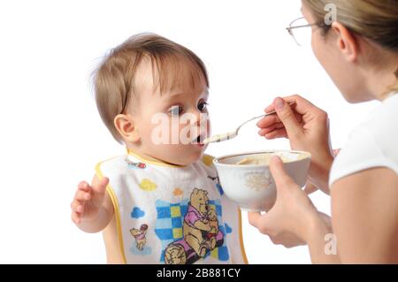 J'ai surpris une petite fille de bébé qui mange de la nourriture à partir de la cuillère. Plaque de maintien de la mère et enfant d'alimentation. Isolé sur fond blanc Banque D'Images