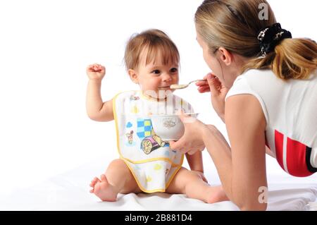 J'ai surpris une petite fille de bébé qui mange de la nourriture à partir de la cuillère. Plaque de maintien de la mère et enfant d'alimentation. Isolé sur fond blanc Banque D'Images