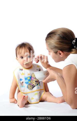 J'ai surpris une petite fille de bébé qui mange de la nourriture à partir de la cuillère. Plaque de maintien de la mère et enfant d'alimentation. Isolé sur fond blanc Banque D'Images