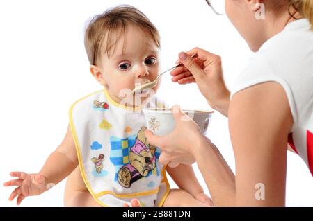 J'ai surpris une petite fille de bébé qui mange de la nourriture à partir de la cuillère. Plaque de maintien de la mère et enfant d'alimentation. Isolé sur fond blanc Banque D'Images