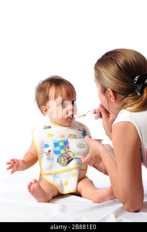 La mère nourrit la petite fille surprise de la nourriture de bébé de la cuillère. Soins parentaux et bonne enfance. Isolé sur fond blanc Banque D'Images