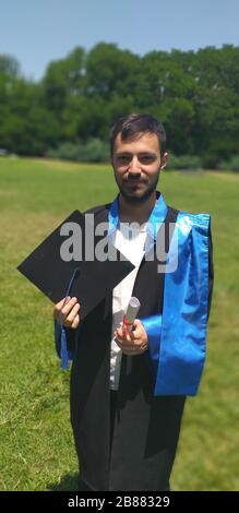 Le jeune diplômé est titulaire de son diplôme et de son plafond de graduation dans un champ Grassy - photo verticale Banque D'Images