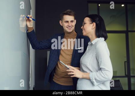 Les jeunes collègues d'affaires font des notes sur le tableau blanc et préparent un rapport en équipe pour la présentation au bureau Banque D'Images