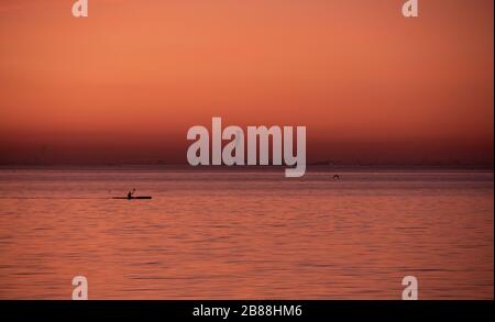 Un homme avide un canoë sur la mer alors que le ciel et l'eau sont colorés en orange et rose pendant un coucher de soleil d'été à Malmö, en Suède Banque D'Images