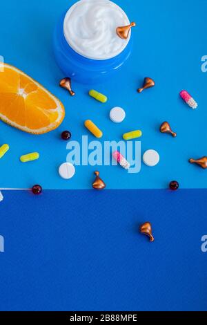 composition flatte lumineuse avec huile, pilules, vitamines, capsules, crème pour le visage, agrumes et oranges sur fond bleu. Concept beauté vitamine naturelle Banque D'Images