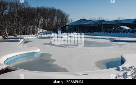 Vue sur l'arrière-cour d'une maison privée ou sanatorium avec piscine ou source chaude couverte de neige sur fond d'arbres à feuilles caduques o Banque D'Images