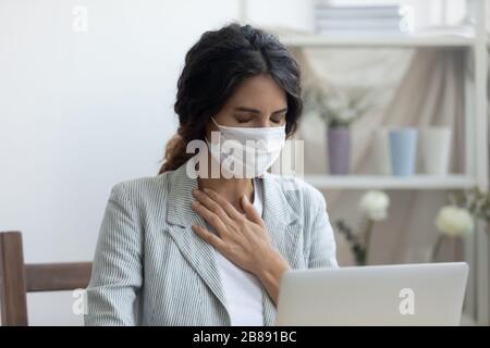 La femme d'affaires dans le masque assis sur le bureau de travail se sent malsaine Banque D'Images