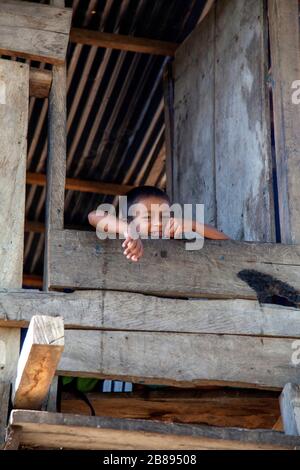 Un garçon indien qui regarde hors de la porte ouverte d'une maison étouffée.Amazone, Colombie et Pérou frontière, Amérique du Sud. Banque D'Images