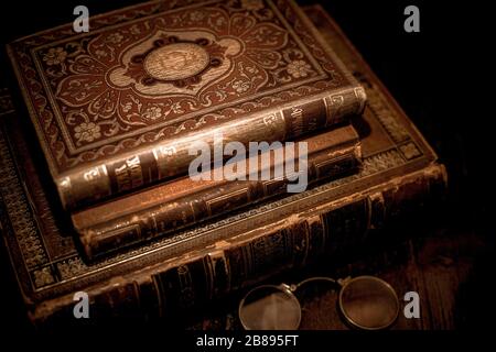 Une pile vintage de trois vieux livres en cuir brun avec des lunettes de vue sur une table en bois. Banque D'Images