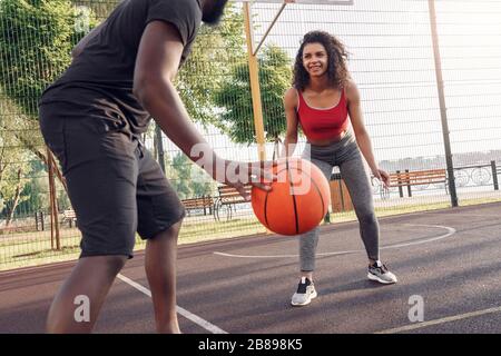 Activités en plein air. Couple africain jouant au basket-ball sur le terrain dribbling fille souriante gaie Banque D'Images