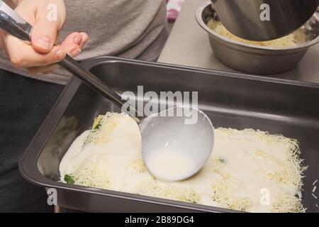 Verser de la sauce crémeuse blanche avec une laque sur des lasagnes d'épinards crus Banque D'Images