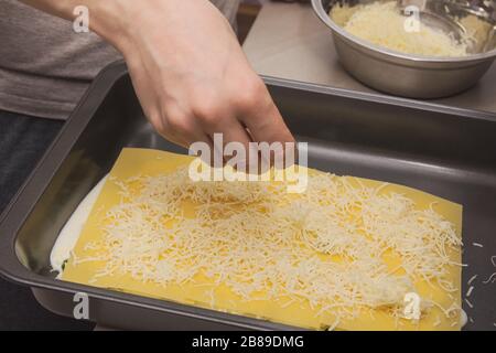 Femme de ménage mettant à la main du fromage râpé sur les lasagnes brutes Banque D'Images