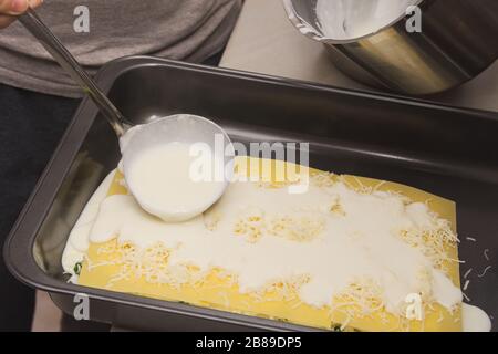 Verser de la sauce crémeuse blanche avec une laque sur des lasagnes d'épinards crus Banque D'Images