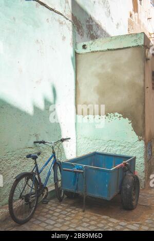 Un vélo et un chariot bleu garés contre un mur vert Banque D'Images