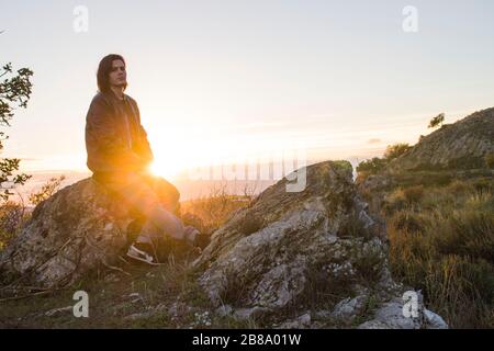 Guy avec de longs cheveux assis sur un rocher. Banque D'Images