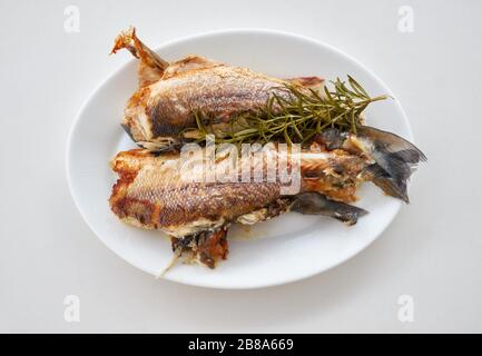 Les deux poissons de mer frits avec une branche de romarin sur une plaque ovale blanche. Banque D'Images